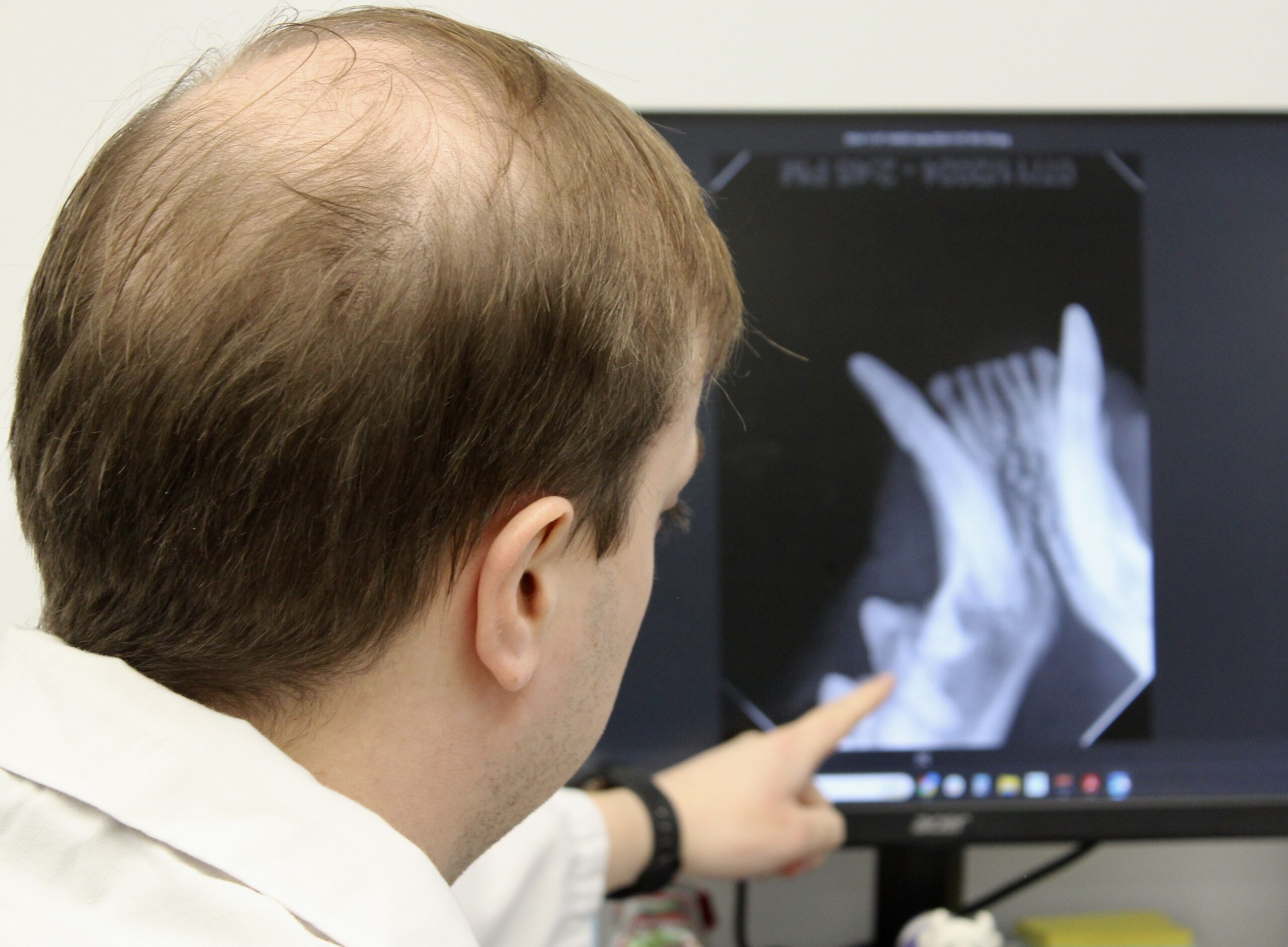 A veterinary technician in a mask and gloves positioning an X-ray machine over a sedated dog on an exam table.